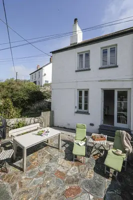 a patio with a table and chairs in front of a house at Coastguard Cottage - set in an elevated position with fabulous views overlooking Portloe in Portloe