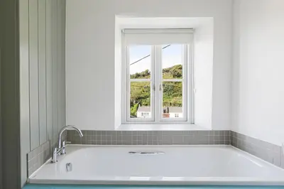 a bath tub in a bathroom with a window at Coastguard Cottage - set in an elevated position with fabulous views overlooking Portloe in Portloe