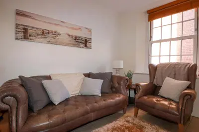 a living room with a brown couch and two chairs at Chapel Cottage in St Austell