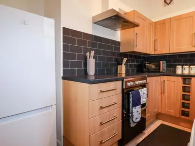 a kitchen with wooden cabinets and a black tile wall at Chapel Cottage in St Austell