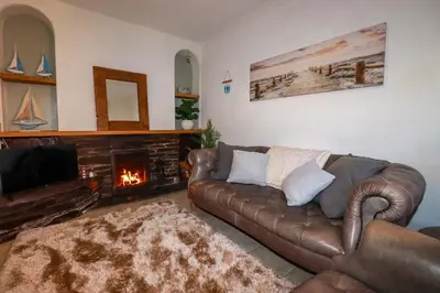 a living room with a leather couch and a fireplace at Chapel Cottage in St Austell