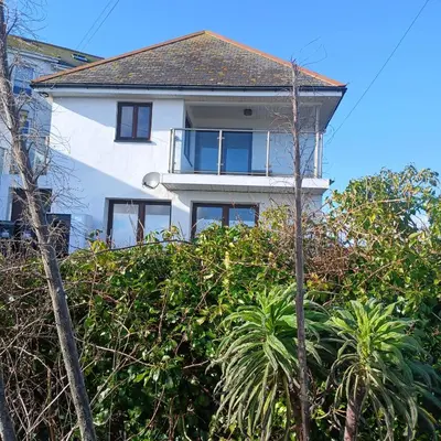 a white house behind some trees and bushes at Harbour Views, Coverack in Helston