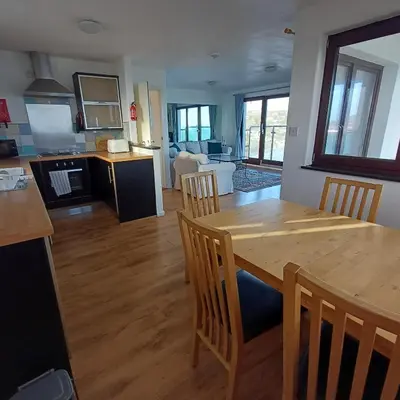 a kitchen and living room with a wooden table and chairs at Harbour Views, Coverack in Helston