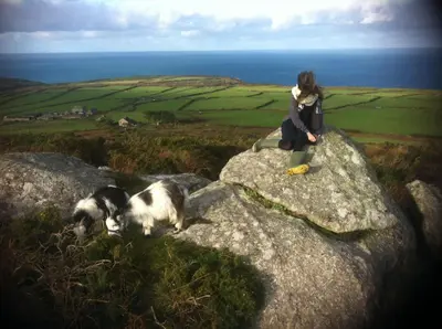 a woman sitting on top of a rock with a dog at The Little Barn Near St Ives Beaches & Walks, Dog Friendly in St Ives