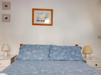 a bed with a blue bedspread and a picture on the wall at Seaside Apartment in Looe