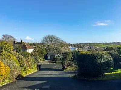 a road with bushes and a house in the distance at Hillside in St Austell