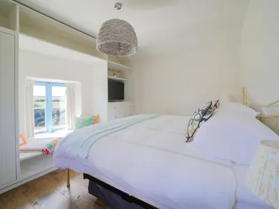 a white bedroom with a bed and a window at Bospebo Cottage in Camborne