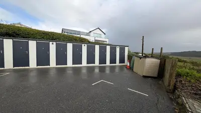 a parking lot with a fence and a building at White Lodge Ocean View Apartment Mawgan Porth in Mawgan Porth