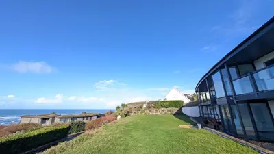 a house on a hill next to the ocean at White Lodge Ocean View Apartment Mawgan Porth in Mawgan Porth