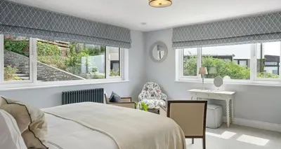 a bedroom with a bed and a desk and windows at Luxury seaside home - 5 mins walk to beach - hot tub in Downderry