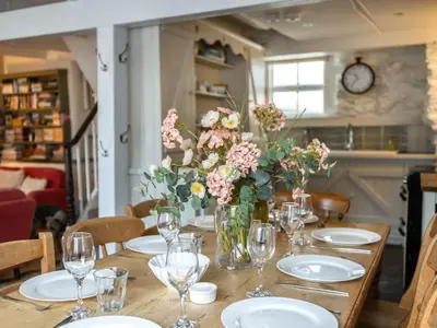 a wooden table with plates and vases of flowers at Geranium Cottage in Port Isaac