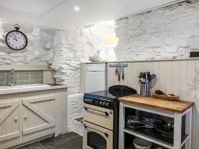 a kitchen with a stove and a clock on the wall at Geranium Cottage in Port Isaac