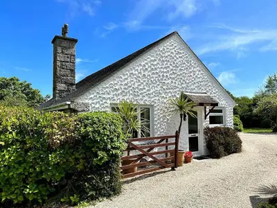 a white cottage with a wooden fence in front of it at Meadow Barn in Coverack