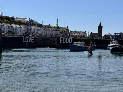 a person on a paddle board in the water with boats at Harbour Hideaway, Porthleven in Porthleven