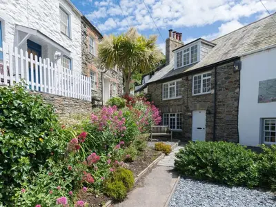a stone house with a white fence and flowers at Poplar Cottage in Port Isaac