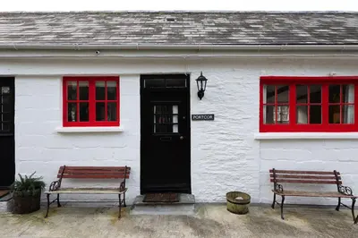 two benches in front of a white house with red windows at Portcor in Port Isaac