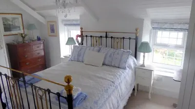 a bedroom with a bed and a dresser and two windows at Trewetha Cottage Bed & Breakfast in Port Isaac