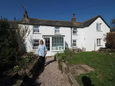 a woman standing in front of a white house at Trewetha Cottage Bed & Breakfast in Port Isaac