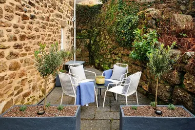 a patio with white chairs and a table and a wall at Finest Retreats - Mill Stone Cottage in Nancledra