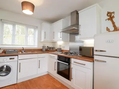 a kitchen with white cabinets and a washer and dryer at Poldam in St Austell