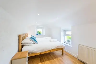 a bedroom with a bed with white sheets and blue pillows at Cornwall Holiday Home with Hot Tub & Sea views in St Merryn