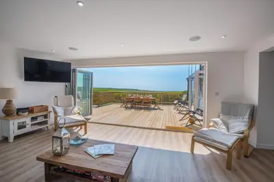 a living room with a view of a deck at Cornwall Holiday Home with Hot Tub & Sea views in St Merryn