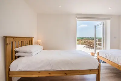 two beds in a bedroom with a view of a patio at Cornwall Holiday Home with Hot Tub & Sea views in St Merryn