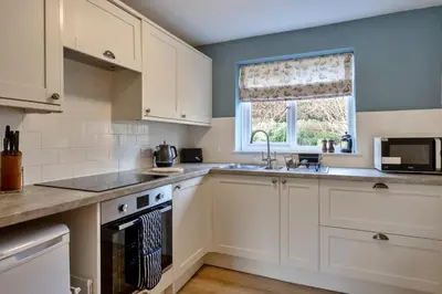 a kitchen with white cabinets and a sink and a window at Finest Retreats - Smugglers Loft at Mixtow Creek in Lanteglos