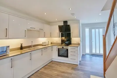 a kitchen with white cabinets and a wooden floor at 2022 Two Bed Stylish House Near Beach in Hayle