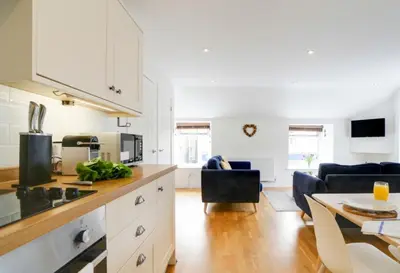 a kitchen with white cabinets and a living room at Harbour Front Flat in Porthleven - Next to shops in Porthleven