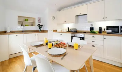 a white kitchen with a table and white cabinets at Harbour Front Flat in Porthleven - Next to shops in Porthleven