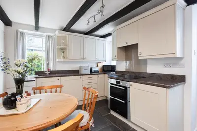 a kitchen with white cabinets and a wooden table at White Pebble Cottage popular village - Port Isaac in Port Isaac