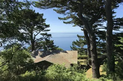 a house with a view of the ocean through trees at Windwhistle coastal views of Looe Bay cliffs in Saint Martin
