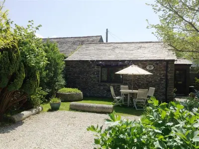 a patio with an umbrella and a table and chairs at Treveglos Barn on the coast road close to Harlyn Bay and Padstow. in St Merryn