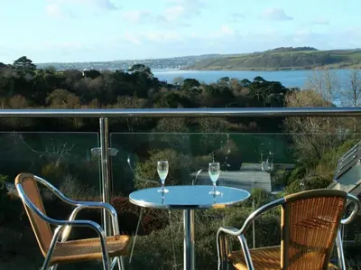 a table and chairs on a balcony with a view of a lake at Pentref St Just in Roseland with beautiful views in Saint Just in Roseland