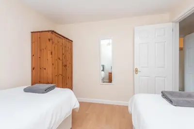 a white bedroom with two beds and a wooden cabinet at Atlantic View Mawgan Porth with sea views in Saint Mawgan
