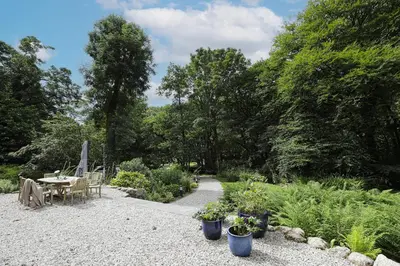 a garden with a table and chairs and plants at Dippers woodland setting at the Luxulyan Valley in Luxulyan