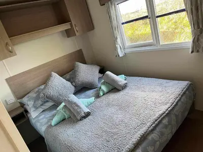 a bedroom with a bed with pillows and a window at Static Caravan 9 in Lansallos