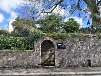 a gate in a stone wall with a sign on it at Bankside Bed & Breakfast in St Austell