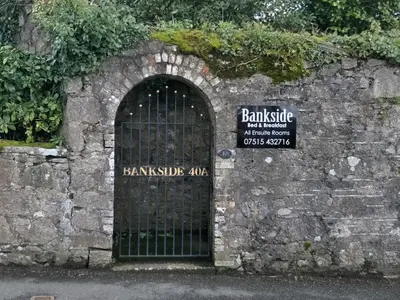 a gate in a stone wall with a sign behind it at Bankside Bed & Breakfast in St Austell