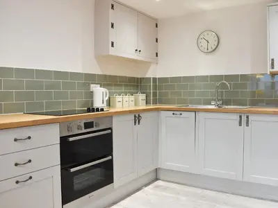 a kitchen with white cabinets and a clock on the wall at Ash in Scorrier