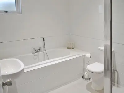 a white bathroom with a tub and a toilet at Sand Dunes in Tywardreath