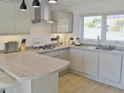 a kitchen with white cabinets and a large island at Sand Dunes in Tywardreath