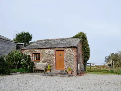 a small stone house with a wooden door and a bench at Nellys House in St Merryn