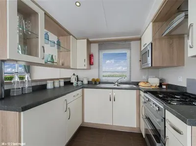 a kitchen with white cabinets and a stove top oven at Widemouth Bay Caravan Park in Bude