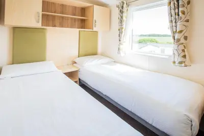 two beds in a small room with a window at Trelawne Manor Holiday Park in Looe