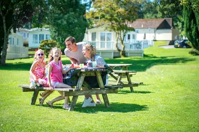 a man and two girls sitting at a picnic table at Trelawne Manor Holiday Park in Looe