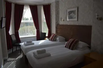two beds in a hotel room with red curtains at Cotswold House in Falmouth