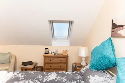a bedroom with a bed with blue pillows and a window at Bosayne Guest House in Tintagel