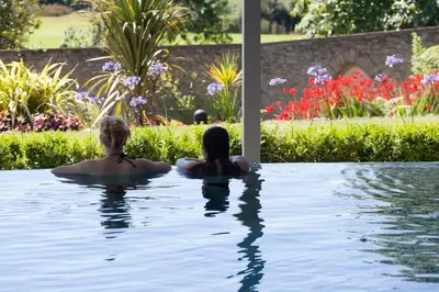 two people sitting in a swimming pool in a garden at The Cornwall Hotel Spa & Lodges in St Austell